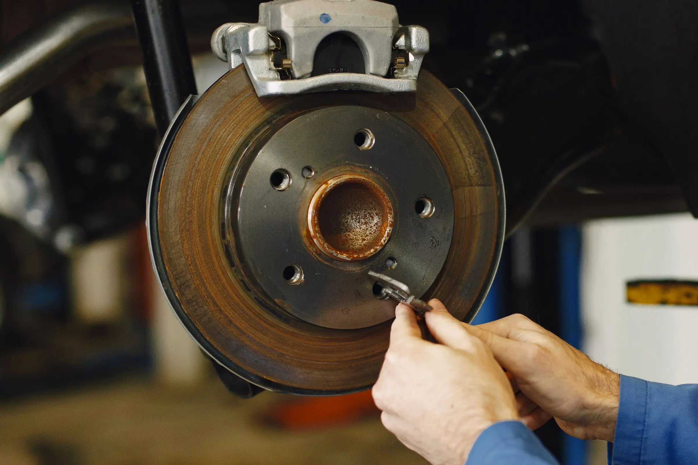 Mechanic’s hands working on a brake rotor and caliper, blue work shirt, car on a lift